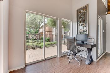A room with a desk and chair in front of a sliding glass door.
